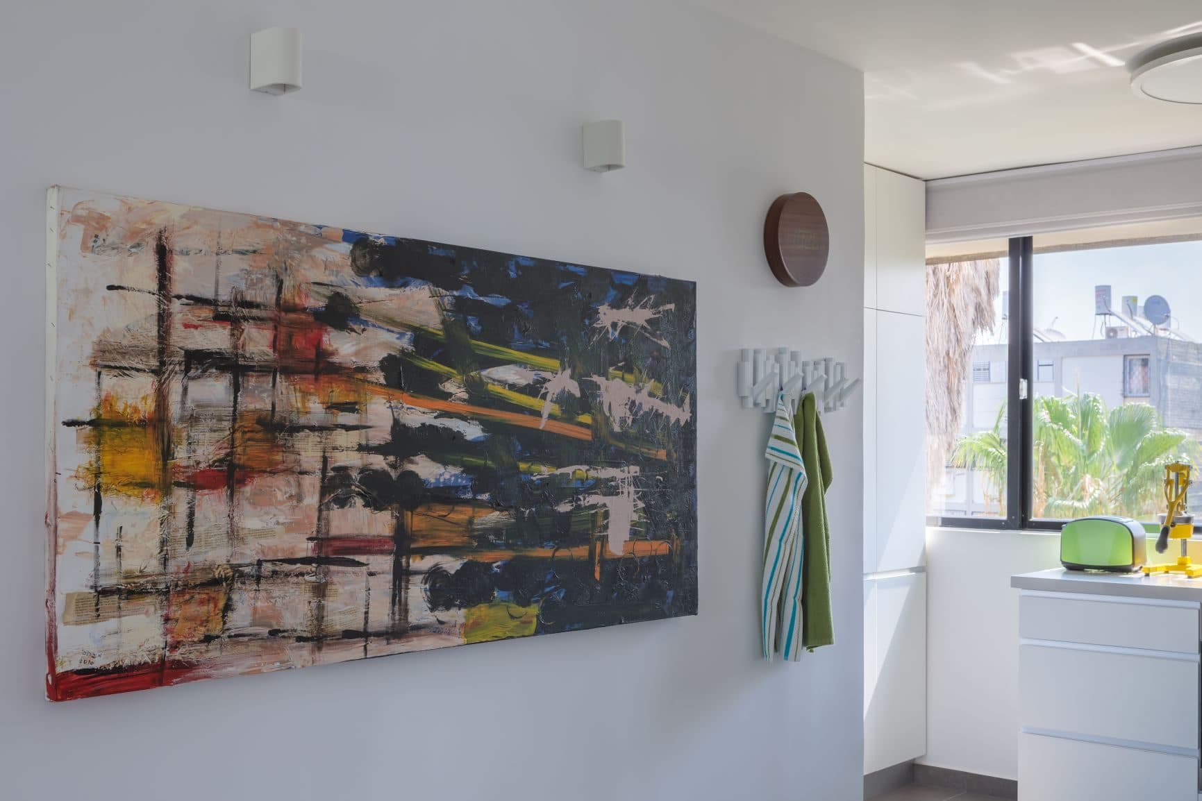 כניסה בנחל עוז יפו, ציור מופשט צבעוני על הקיר לצד קולב עם סוודר ירוק וחלון לנוף