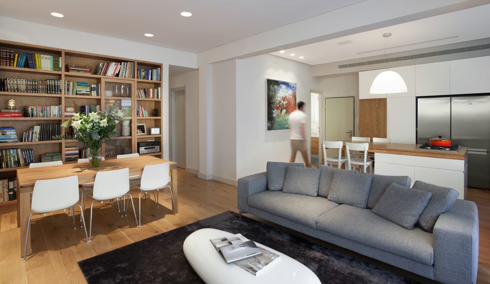 מבט פתוח מהסלון למטבח ולפינת האוכל בדירת צייטלין, דלת הזזה מחוברת למרפסת ירוקה מוצללת ווילון שקוף