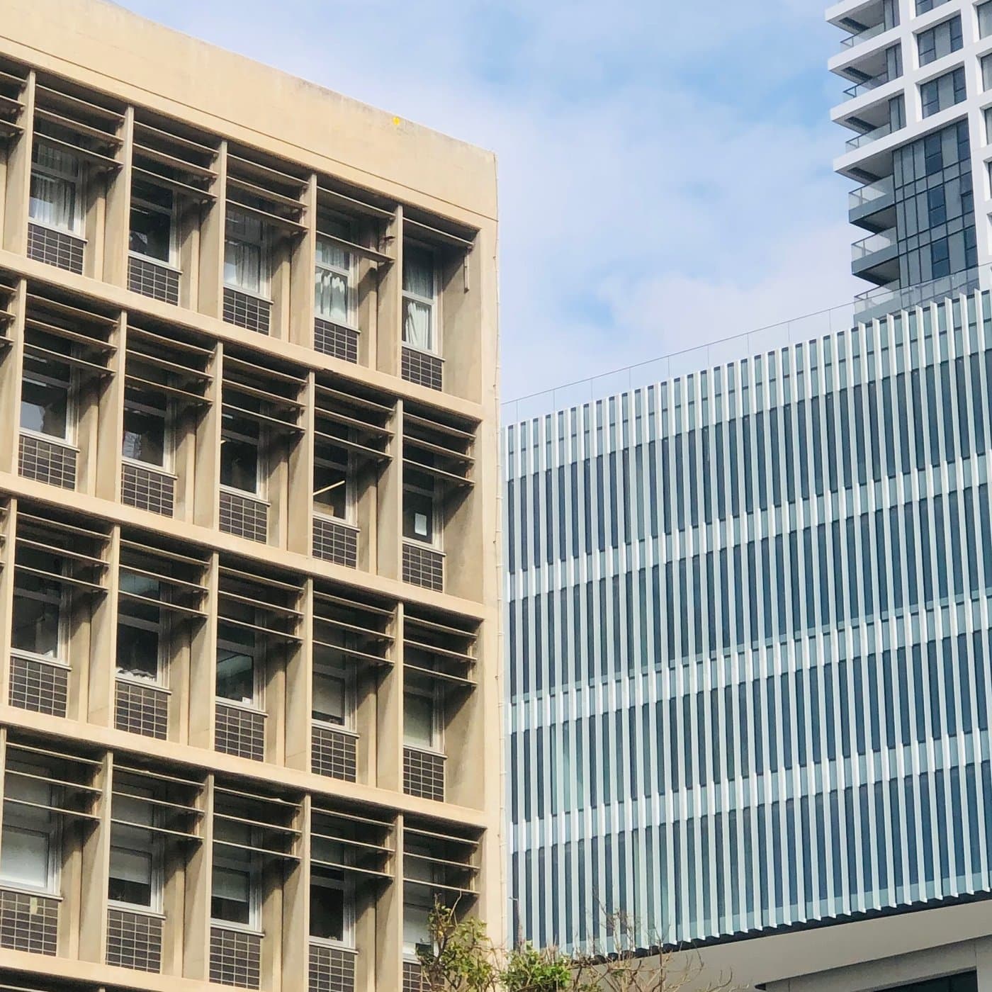 חזית בניין ברוטליסטי מבטון חשוף עם רשת חלונות שקועים, מול מגדל זכוכית עכשווי