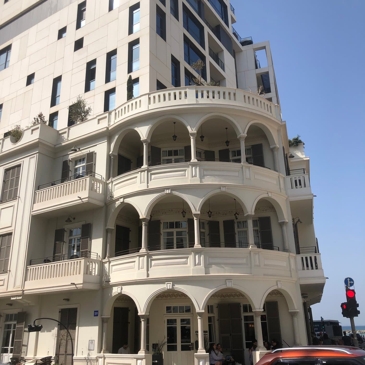 בניין אקלקטי משופץ עם שלוש קומות מרפסות קשתיות, מול מגדל מגורים לבן מודרני ברחוב עירוני סואן