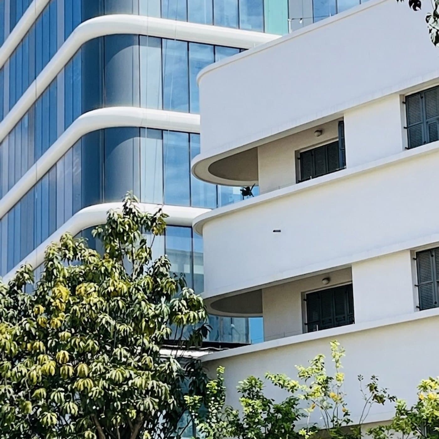 בניין באוהאוס לבן עם מרפסות מעוגלות מול מגדל זכוכית כחול עכשווי עם קווי מרפסות מהדהדים