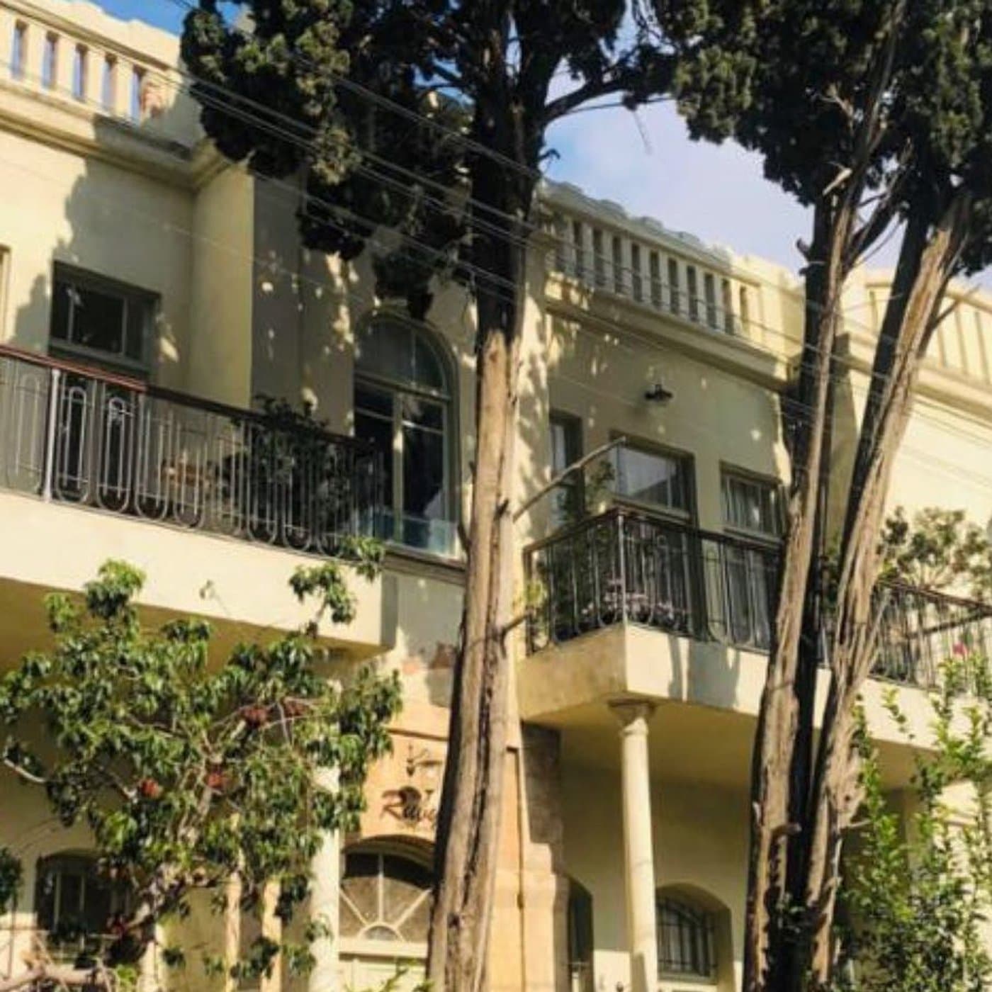 בניין אקלקטי ברחוב יהודה הלוי, תריסי עץ ומעקות ברזל מפותלים על המרפסות מול עצים גבוהים