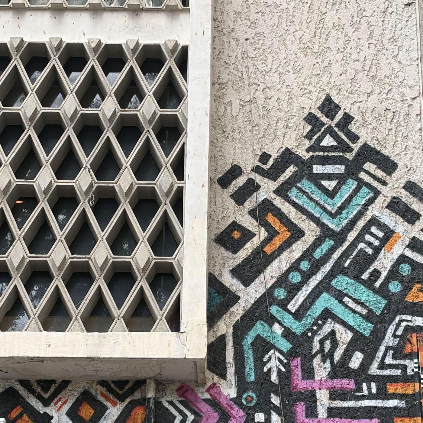 מסך בטון מחורר בדוגמת מעוינים לצד ציור קיר גרפי בטורקיז, כתום וורוד, בכיכר מיכאל'ס